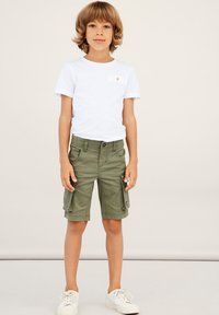 White short-sleeve t-shirt and olive green cargo shorts. Shorts feature side pockets, a button closure, and a casual fit. White sneakers.