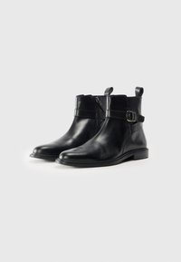 Botas de cuero negras hasta el tobillo con puntera redondeada, cierre de cremallera lateral, correa ajustable con hebilla y tacón plano. Textura suave y diseño minimalista.