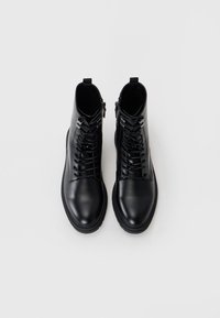 Botas de tobillo de cuero negro con una textura suave. Con cordones en la parte frontal y una cremallera lateral para el cierre. Suela de goma duradera.