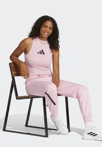 Rosa atletisk klädsel med en ärmlös topp med svart logotyp och matchande joggers med svarta accenter, i kombination med vita sneakers.