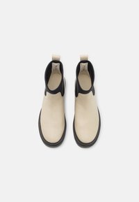 Paire de bottines beige et noire avec languettes et semelles plates noires vues de dessus sur fond blanc.