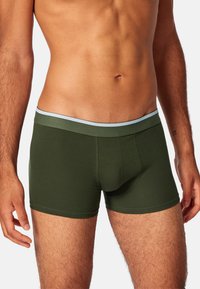 Mörkgröna boxertrosor med ett ljusblått elastiskt midjeband. Tyget ser mjukt ut med en slät textur och en figursydd design.