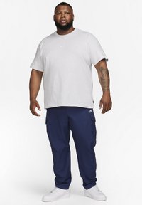 Grijze t-shirt met korte mouwen en het Nike-logo, gecombineerd met navy cargobroek met zakken, aangevuld met witte sneakers.