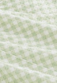 Tissu à carreaux verts et blancs avec un tissage texturé, présentant un motif à petite échelle. Le tissu tombe doucement, révélant des plis souples.