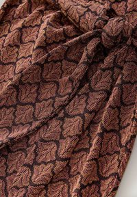 Textilie s černým základem zdobená strukturovaným, kovovým vzorem v tmavě růžové a zlaté barvě. Látka má jemný, tkaný vzhled.