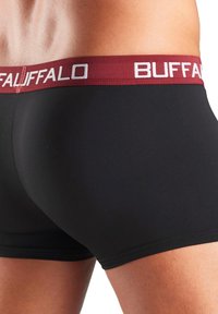 Melnas bokseru bikses, kas izgatavotas no gludas auduma, ar bordo krāsas jostu, kurā baltā krāsā ir uzraksts "BUFFALO". Vidējas garuma, līdz augšstilbam, un pieguļošs dizains.