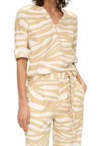 Camicia a righe beige e bianca con scollo a V, maniche corte arrotolate e pieghe sottili, realizzata in tessuto leggero. Abbinata a pantaloni coordinati.