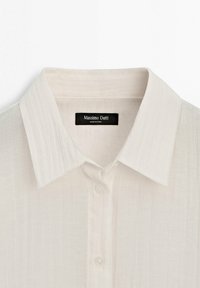 Chemise blanche à col boutonné avec des fines rayures verticales et une étiquette noire "Massimo Dutti" cousue à l'intérieur du col.