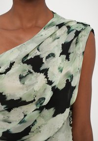 Ženska brezrokavna obleka iz lahkega materiala, okrašena z zelenim cvetličnim vzorcem na črni podlagi, z drapirano ovratnikom in gumbnimi detajli.