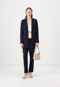 Námořnický blazer se zlatými knoflíky, v kombinaci s květinovou blůzou a námořnickými kalhotami. Drží béžovou kabelku. Viditelné otevřené lodičky v tělové barvě.