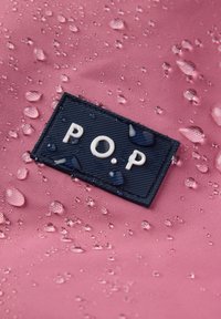 Waterdruppels op roze waterproof stof met een gestikte zwarte rechthoekige patch met het label "P.O.P" in witte letters.