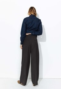 Chemise en denim noir à manches longues, associée à un pantalon large taille haute gris foncé et des chaussures à imprimé animal. Vue de dos.