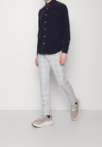 Marinblå kordflöjelskjorta med knappar, grå rutiga slim-fit byxor och beige sneakers med texturerade detaljer och tjocka vita sulor.