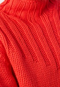 Fester roter Strickpullover mit hohem Kragen, der strukturierte vertikale Streifen und erhabene Abschnitte aufweist, aus dicker Wolle gefertigt.