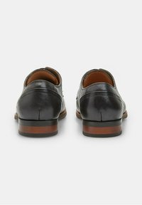 Chaussures en cuir avec une finition noire lisse, un talon de hauteur intermédiaire et des accents marron, dotées d'un bout arrondi et d'un intérieur rembourré.
