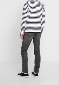 Chemise à rayures noires et blanches à manches longues, jeans gris et baskets noires. La chemise présente un col rond et une silhouette ajustée.