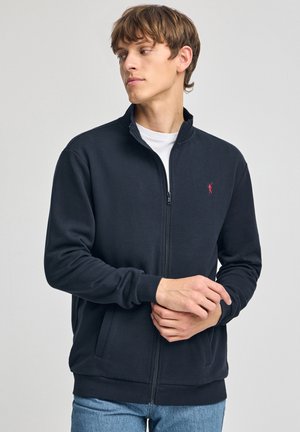 Donkerblauwe zip-up sweatshirt van zacht materiaal, met een opstaand kraag, twee zijzakken en een klein rood logo op de borst.