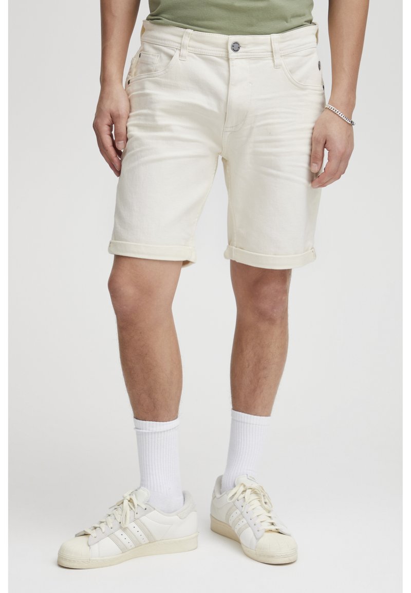 Hvite denimshorts med rullekanter, fem lommer og metallknapplukking, kombinert med hvite sneakers og ankelsokker.