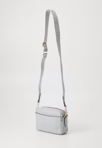 Borsa a tracolla in pelle grigia con forma rettangolare, chiusura a zip e una tracolla testurizzata con logo "BOSS" in una stampa sottile. Accenti dorati.