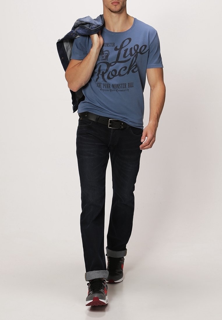 Modrá tričko s černým textem "Live Rock", tmavé džíny s ohrnutými manžetami a černé tenisky s červenými detaily. Džínová bunda přehozená přes rameno.