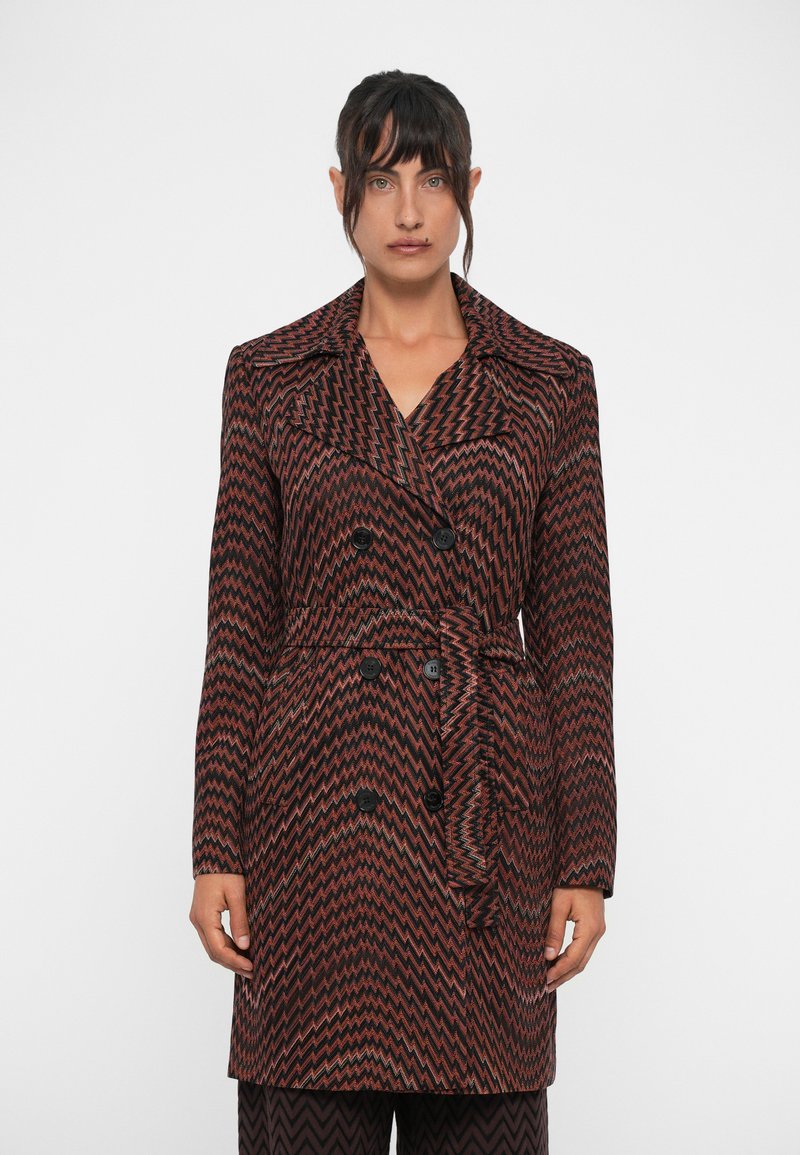 Manteau à motif zigzag marron et noir avec design croisé, grand col et détail de ceinture. Comprend des boutons noirs.