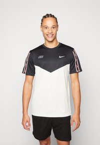 Camiseta deportiva Nike para hombre con la parte superior negra, la parte inferior blanca y franjas laterales con acentos rojos. Presenta un escote redondo y logotipos.