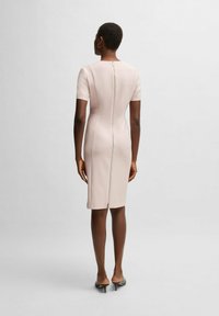 Abito fitted rosa pallido con maniche corte e zip sul dietro. Texture liscia, lunghezza al ginocchio e design minimalista.