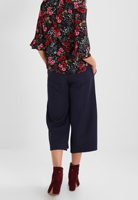 Blusa floreale con sfondo nero, maniche a tre quarti a campana; abbinata a culotte navy e stivaletti con tacco borgogna.
