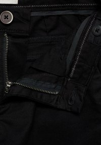 Jeans en denim noir avec fermeture à bouton en métal et zip. Présente des coutures et une taille contrastantes, une texture lisse et des poches latérales.