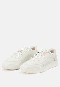 Weiße Leder-Sneaker mit einem schlanken Design, runder Zehenpartie, Schnürverschluss an der Vorderseite und einem dezenten roten Akzent an der Seite. Dicke weiße Gummisohle.