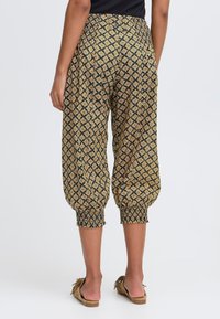Pantalons harem à motif noir et or avec un waistband élastique et des chevilles froncées. Texture douce et coupe ample pour le confort.