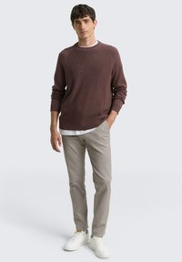 Bordeaux gebreide trui met ribbels aan de mouwen en de hals, gedragen over een wit T-shirt, gecombineerd met lichtgrijze broeken en witte sneakers.