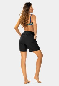 Czarne szorty z elastycznym pasem. Biustonosz w kwiatowy wzór z niebieskimi ramiączkami. Modelka pokazana od tyłu, stojąca boso.