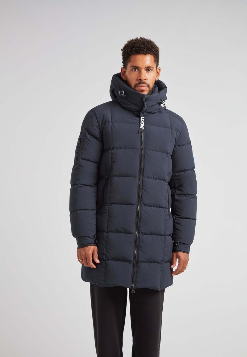 Giubbotto imbottito di colore blu scuro con colletto alto, chiusura con zip e motivo trapuntato. Presenta un cappuccio regolabile e tasche laterali.