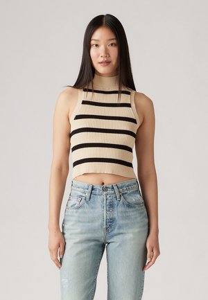 Top corto de canalé beige con rayas horizontales negras, cuello alto y diseño ajustado, combinado con vaqueros de cintura alta en azul claro.