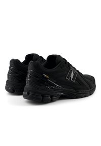 Paire de chaussures de course New Balance noires avec tissu texturé et semelles rembourrées, vues de l'arrière et de profil sur fond blanc.