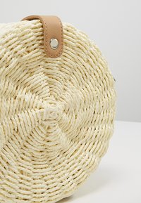 Borsa tonda intrecciata realizzata in corda di colore naturale con una finitura texture, caratterizzata da una tracolla in pelle marrone e una chiusura a scatto metallica.