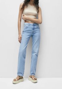 Jeans azzurri chiari a vita alta con un design a gamba dritta, abbinati a un top aderente beige e sandali con plateau color crema.