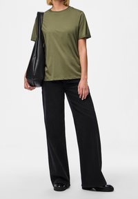 Olivově zelené bavlněné tričko s kulatým výstřihem, doplněné černými širokými kalhotami a strukturovanou černou kabelkou přes rameno, umístěné na bílém pozadí.