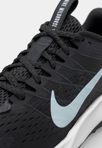 Black athletic shoe with a textured upper, featuring a light blue Nike swoosh logo, black laces, and a white sole.