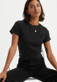 Mustapaitainen lyhythihainen puuvillapaita, jossa on pyöreä pääntie, yhdistetty korkeavyötäröisiin mustiin farkkuihin. Minimalistinen muotoilu.