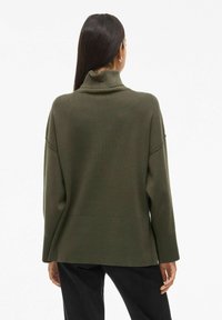 Pull vert olive avec un col haut et une coupe ample. Présente des épaules tombantes et une texture côtelée, avec un ourlet droit en bas.
