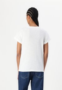 Camiseta blanca de manga corta con puños enrollados, hecha de tejido ligero, que presenta un corte holgado y una superficie texturizada lisa.