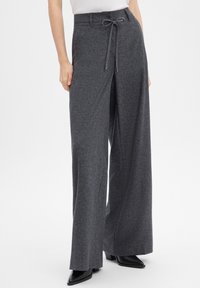 Gray wide-leg pants made of textured fabric, featuring a drawstring waist and minimal hardware, paired with black heeled boots.