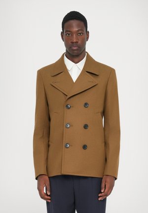 Brun uld peacoat med dobbeltbrystet design, store sorte knapper, påsat krave og sidelommer, båret over en hvid skjorte.