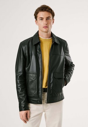 Schwarze Lederjacke mit Kragen, Frontreißverschluss, zwei Brusttaschen und glatter Textur, getragen über einem gelben Pullover.