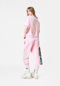 Conjunto de ropa de casa rosa con alas de plumas bordadas en la parte posterior de la camiseta y los pantalones, con puños acanalados. Combinado con botas de combate blancas.