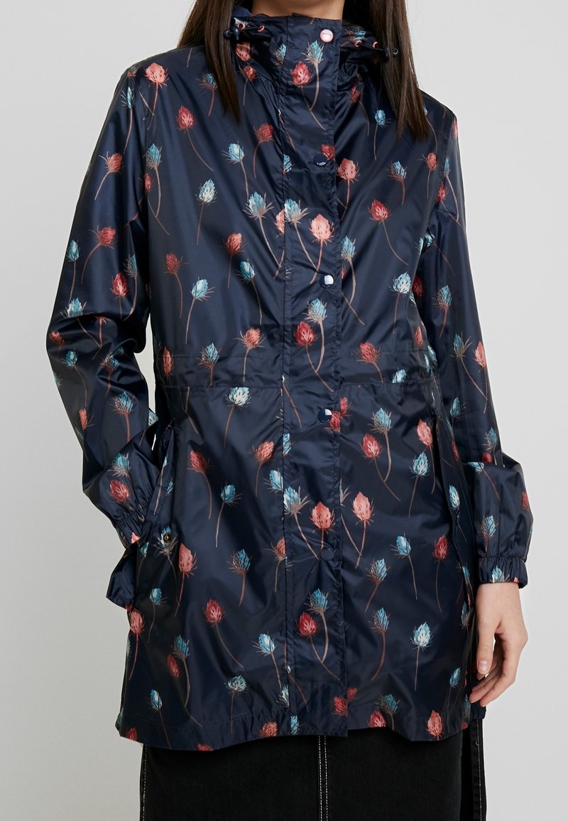 Giacca impermeabile blu navy con motivo floreale in tonalità di rosso e blu, caratterizzata da vita aderente, polsini elasticizzati e cappuccio.