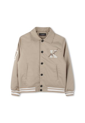 Beige jasje met een kraag, knopen aan de voorkant en twee zijzakken. Heeft een geborduurd "K" en gestreepte accenten op de manchetten. Vrouwelijk textuur.