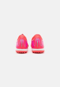 Bright pink soccer cleats with a textured upper, silver accents, and a white midsole. Features an angular design and studded outsole.